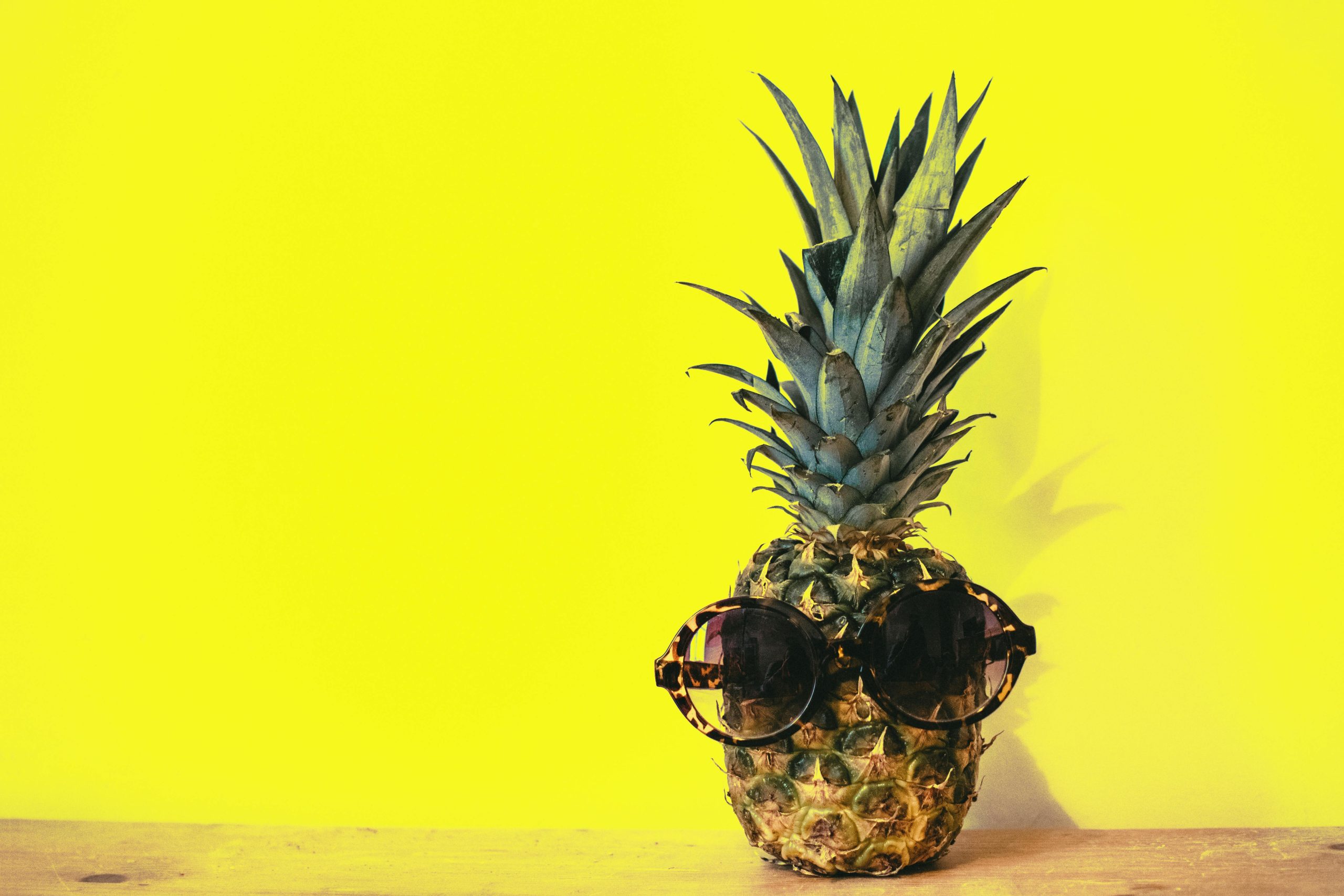 A stylish pineapple wearing sunglasses against a bright yellow background.