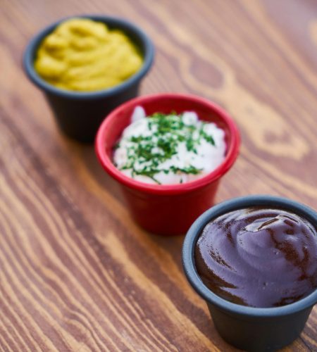About A close-up of three sauces in cups on a wooden surface, arranged in line.