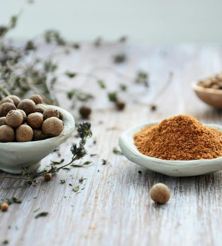About An artistic display of whole and ground spices in ceramic bowls on a rustic wooden surface, emphasizing culinary tradition.